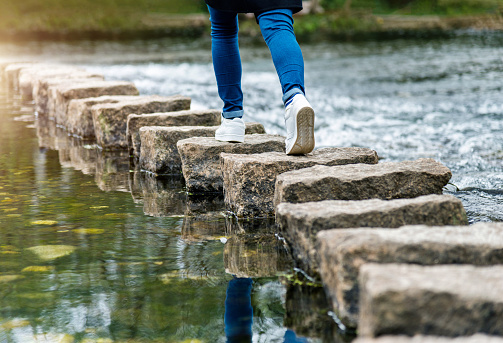 Woman crossing a river on stepping stones.