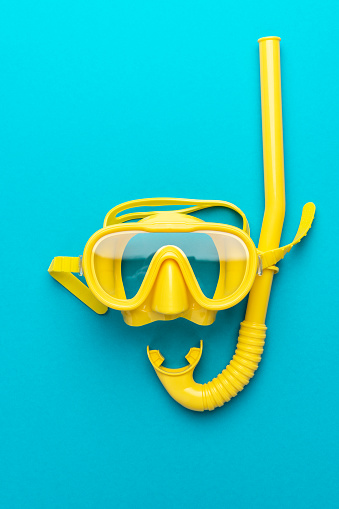 flat lay shot of yellow diving mask with snorkel over blue background. minimal conceptual photo of dive mask and snorkel central composition. flat lay of diving equipment vertical orientation