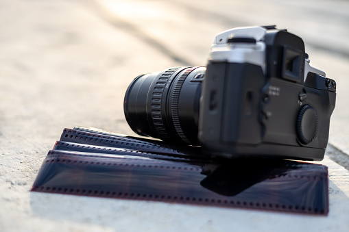 A close-up view of an old black camera and a sheet of film left on the concrete pillars with blurred light bokeh in the background during an afternoon sunset.