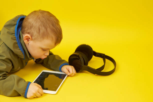 istock A child lying down uses a digital tablet on a yellow background 1362082025