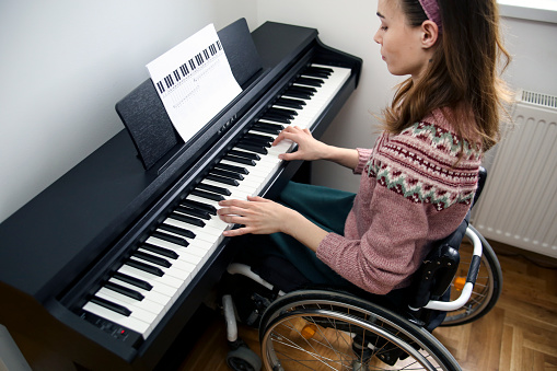 Disabled young woman in a wheelchair playing an electric piano. About 25 years old, Caucasian female.