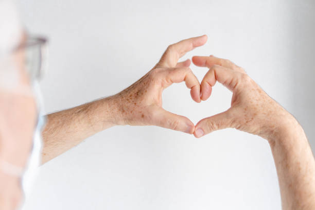 istock elderly man making a heart with his hands, white background, wearing a medical mask 1362087321