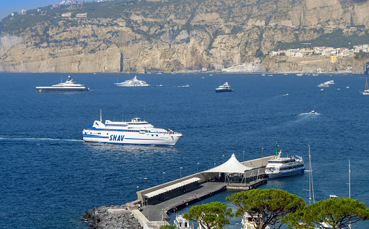 Sorrenbto, Italy - August 2019: Fast ferry operated by SNAV arriving at the port of Sorrento with luxury yachts moored in the bay in the background