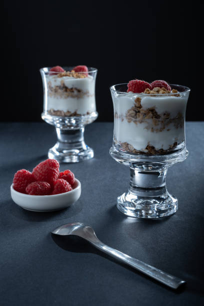 Two glass bowls of vanilla yogurt with cinnamon roll granola and raspberry topping stock photo