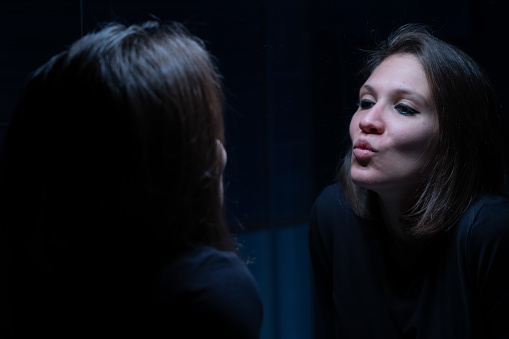 A dark and blue scene where a young woman is seeing his face throughout the bathroom mirror