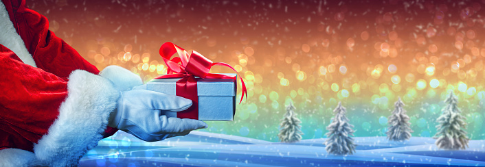 Santa Claus Hand Holding Christmas Gift Box, Snow Background And Winter Time