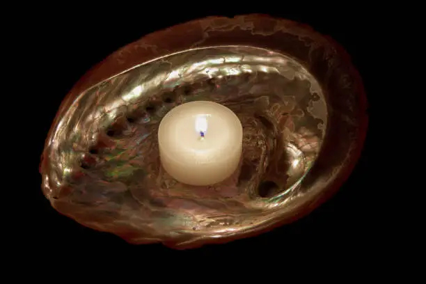 Abalone iridescent  seashell with a lit candle. Black background. Stock Image.