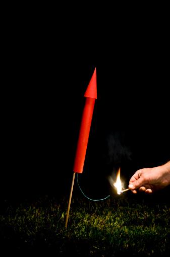 Hand with match lighting a Red firework/rocket fuse