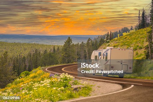 istock Camper Driving Down Road in The Beautiful Countryside Among Pine Trees and Flowers. 1362129184