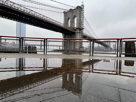 Reflections of Brooklyn Bridge in a puddle  after a storm. View from Manhattan side