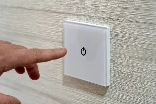 save energy concept, closeup of finger touching to electric switch. a man's finger presses a touch-sensitive modern switch on a white wall.