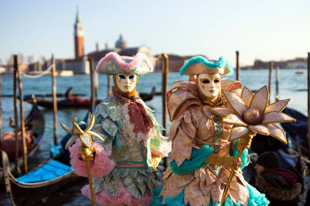 Venice carnival masks couple Venice, Veneto, Italy - February 19, 2020: Colourful and beautifully crafted costumes for this couple posing at San Marco square waterfront at sunset. venice stock pictures, royalty-free photos & images