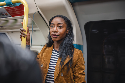 Young adult black woman passenger in brown jacket holding to handrail on London underground train