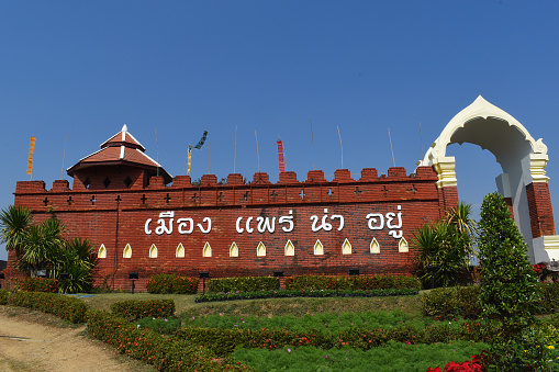 Building at the Entrance to Phrae, Den Chai District, Northwest Thailand, half Part of a historical Monument, Brick Building and Gate, Battlements, covered Station for the Guards, Flags, Garden, Attraction, Point of Interest