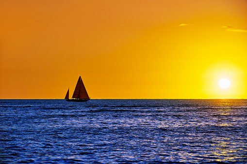 One sailboat sailing at sunset horizon over sea, Hawaii, USA.