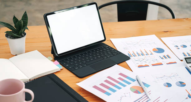 istock Mockup blank screen portable tablet with magic keyboard and papaerwork, graph, chart on wooden table. 1362177650