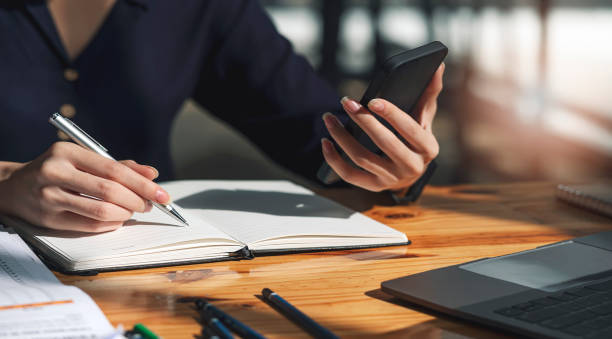 istock Businesswoman using smartphone and writing note, planning and analyzing investment or marketing, stock business and work from home concept. 1362177664
