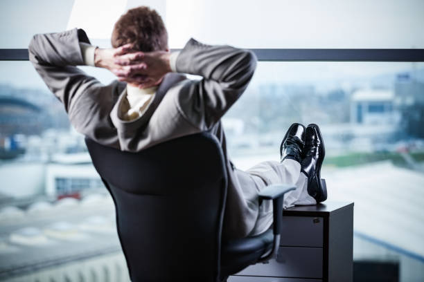 istock Businessman resting putting legs on pedestal looking through glass window 1362180420