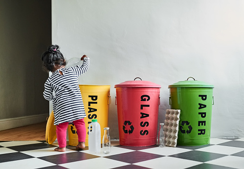 Little girl putting different waste into separate recycling containers at home