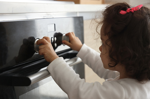 Little girl turns the oven button