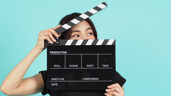 Asian Woman holding black clapperboard and closing face on mint or Tiffany Blue background.