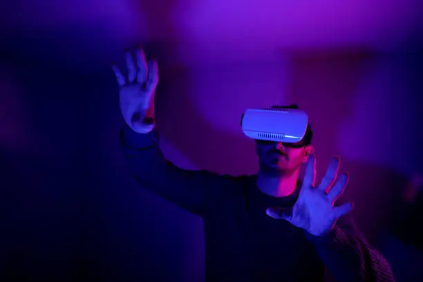 Photo of He is discovering metaverse by using VR glasses under neon lights