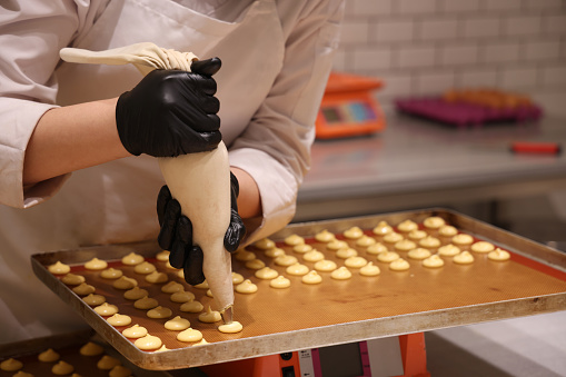 Close-up of a pastry chef with confectionary bag squeezing cream in the pastry shop or bakery