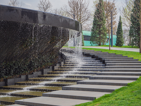 A dry and wet staircase with black granite steps in the park near an artificial waterfall flowing from the fountain bowl into the granite bed of an artificial river.  Krasnodar, Russia  April 27, 2021