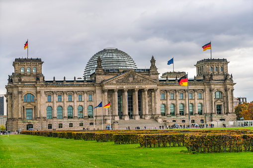 Reichstag building, seat of the German Parliament (Deutscher Bundestag), in Berlin, Germany with trees in autumn color against cloudy sky