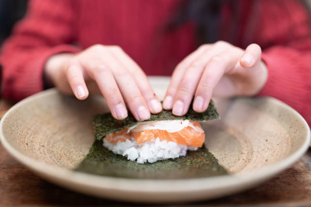 un bambino che prepara sushi arrotolato a mano - temaki food sushi salmon foto e immagini stock