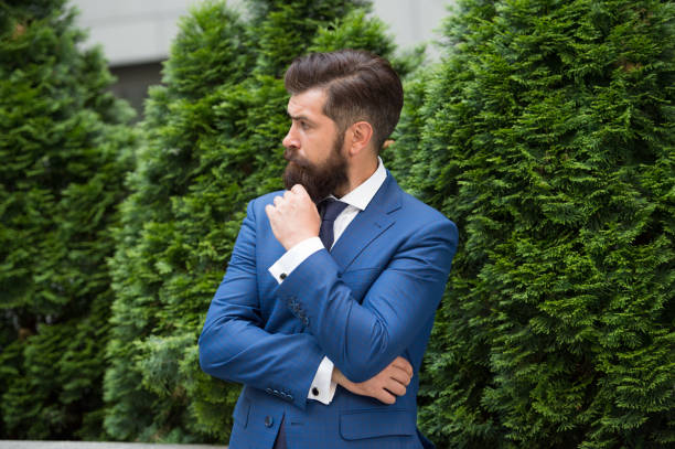 vêtements pour hommes. concept d’efficacité énergétique. homme barbu en veste près du cyprès. bel homme habillé intelligemment. ceo marcher dans la rue. homme d’affaires marchant à l’extérieur. homme d’affaires dans la nature - natural bristle audio photos et images de collection