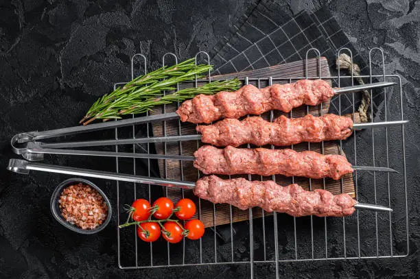Raw Shish kebab from mince lamb and beef meat, turkish adana kebab on Skewers. Black background. Top view.
