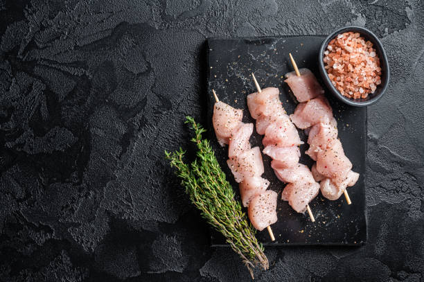 Raw chicken meat shish kebab skewers. Black background. Top view. Copy space