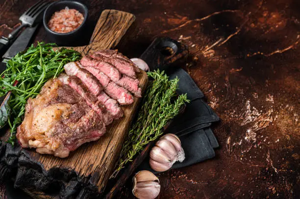 Grilled Chuck Roll beef steak with salad on wooden board. Dark background. Top view. Copy space.