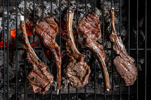 Grilled lamb mutton chop steaks on barbecue, outdoor BBQ grill with fire. Top view.