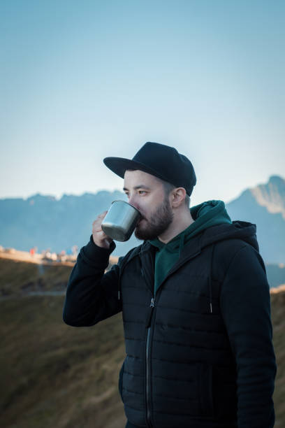 istock Bearded traveler man drinks tea or coffee from  metal cup while resting on a rock 1362224538