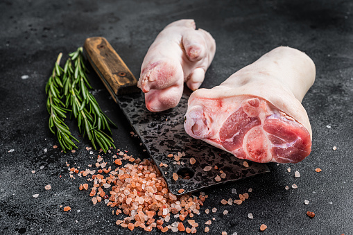 Butcher shop - Raw pork hoof,  knuckle, feet on a cutting board. Black background. Top view.