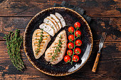Protein dinner - grilled Turkey breast fillet steaks on a plate with tomato. Wooden background. Top view