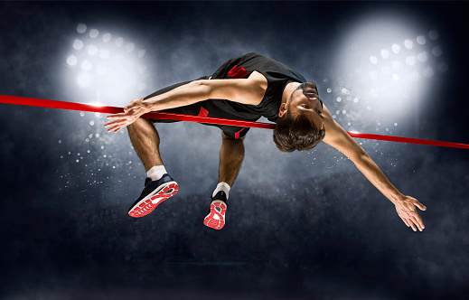 Man in action of high jump a stadium at night. Horizontal copy space background