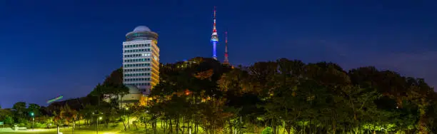 The iconic spire of the N Seoul Tower illuminated at night high on Namsan Mountain overlooking spotlit parkland below in the heart of Seoul, South Korea’s vibrant capital city.