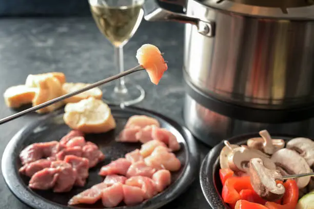 Hot oil fondue with pieces of meat and vegetables, to be fried in a pot with sizzling fat, gregarious festive dinner often served at parties, selected focus, very narrow depth of field