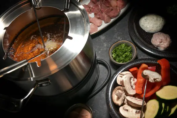 Fondue pot with hot oil, long forks, vegetables and raw meat, festive party dinner for friends and family, selected focus, narrow depth of field