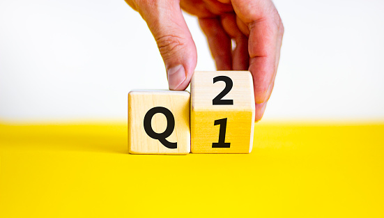 From 1st to 2nd quarter symbol. Businessman turns a wooden cube and changes words 'Q1' to 'Q2'. Beautiful yellow table, white background. Business, happy 2nd quarter Q2 concept, copy space.