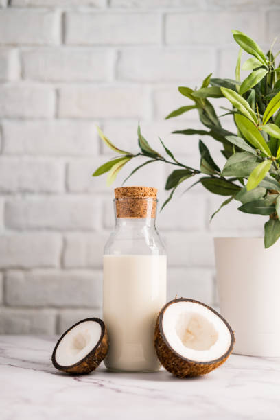 Fresh coconut milk in glass bottle, vegan non dairy healthy drink. Glass bottle with milk on white kitchen table with coconut aside. Coconut kefir in bottles on wooden table. Vegan non dairy healthy or fermented drink. Healthy eating concept. coconut milk stock pictures, royalty-free photos & images