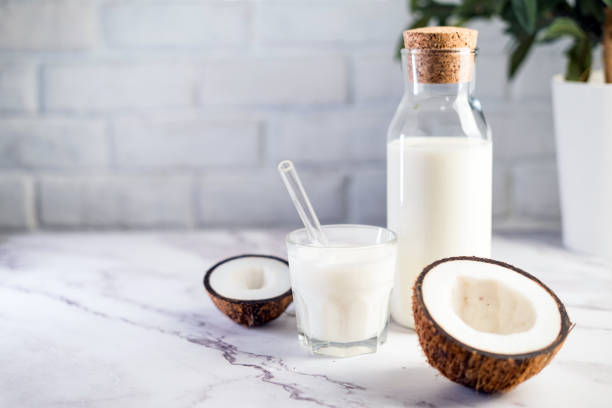 Coconut drink in bottle on white marble table. Glass bottle with milk on white kitchen table with coconut aside.  Vegan non dairy healthy or fermented drink. Healthy eating concept. coconut milk photos stock pictures, royalty-free photos & images