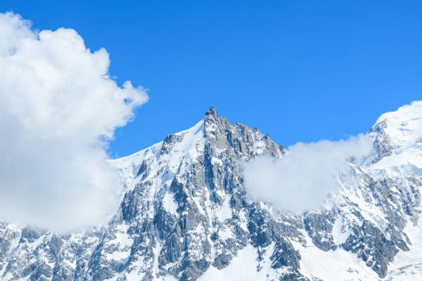 lAiguille du midi sous les nuages dans le massif du Mont Blanc en Europe, en France, dans les Alpes, vers Chamonix, en ete, lors dune journee ensoleillee. stock photo
