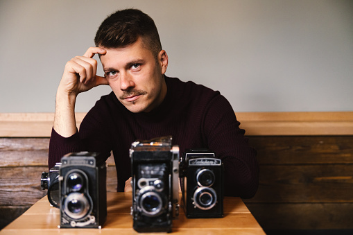 Portrait of a Caucasian man, a small business owner with his collection of analog retro cameras