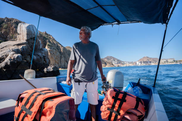 mexikanischer bootskapitän führt touristen an einem sonnigen späten nachmittag zum ikonischen bogen in cabo san lucas, baja california sur, mexiko am meer von cortez pacific ocean - mexico only men senior men mature men stock-fotos und bilder