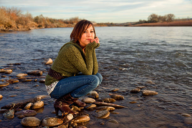 Beautiful young girl sitting on her heels near a rocky riverbank