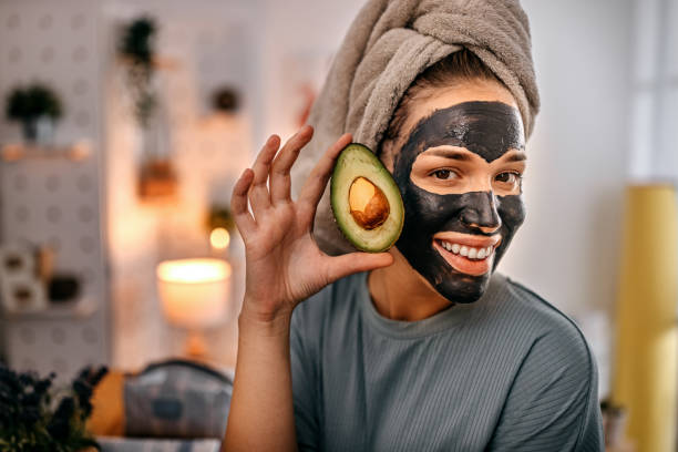 アボカドを保持する黒いフェイスマスクを持つ女性 - peel facial mask human face human skin ストックフォトと画像